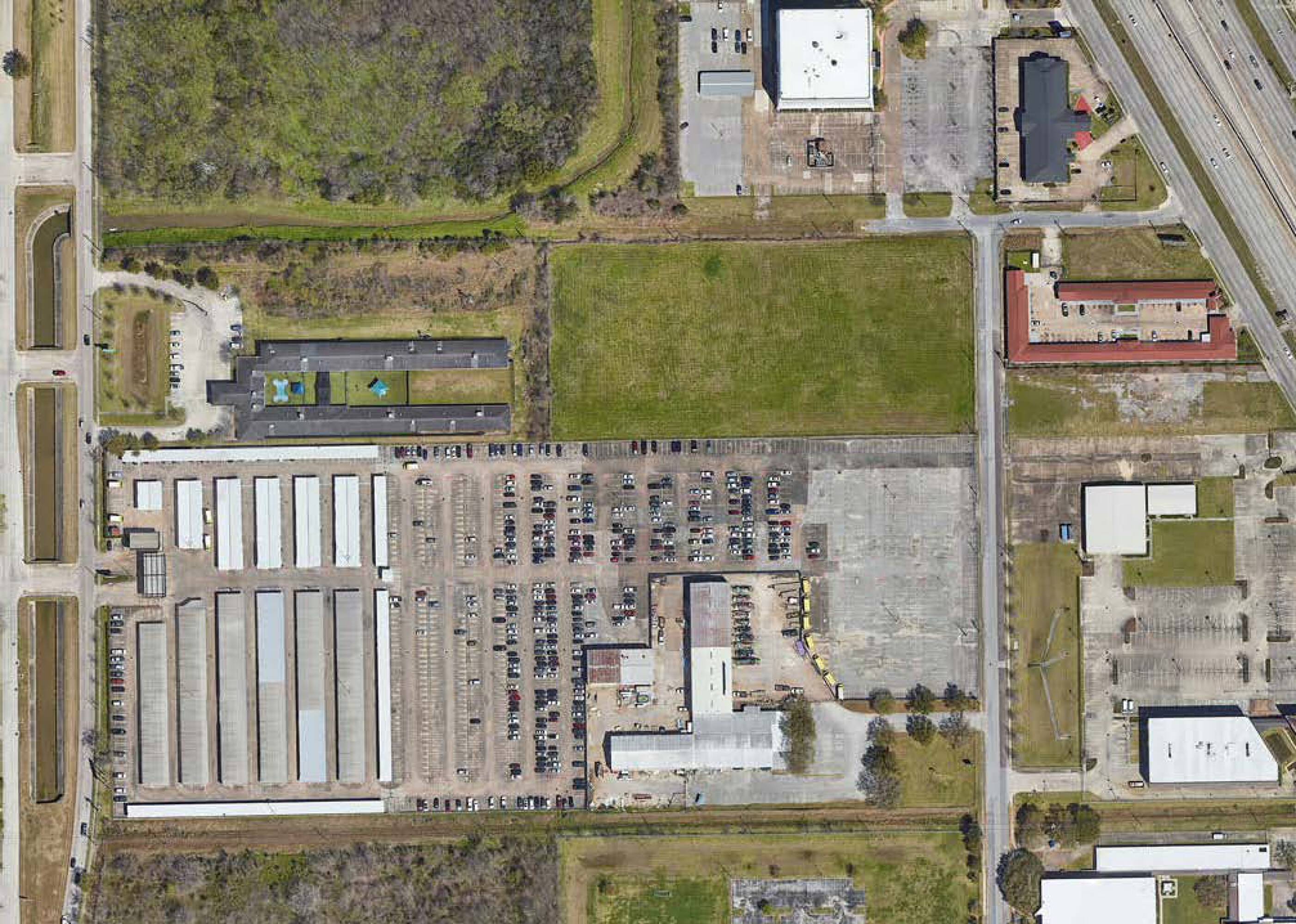 Aerial view of the property at 7625 Monroe Rd, Houston, TX, showing large open land with adjacent commercial and industrial buildings.