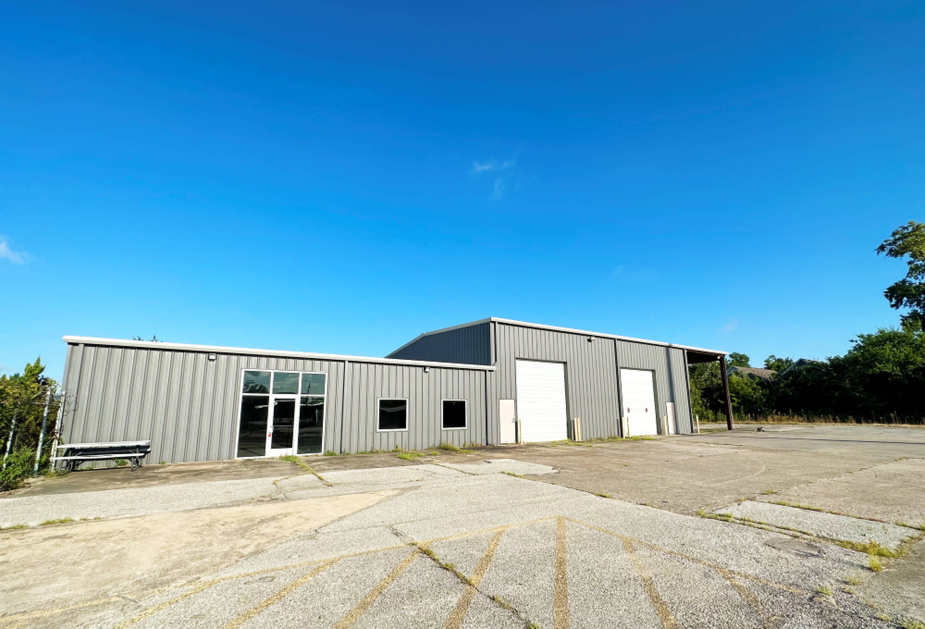 Vacant land with a metal building at 1400 W 20th St, Houston, TX, featuring large windows, garage doors, and ample parking space.