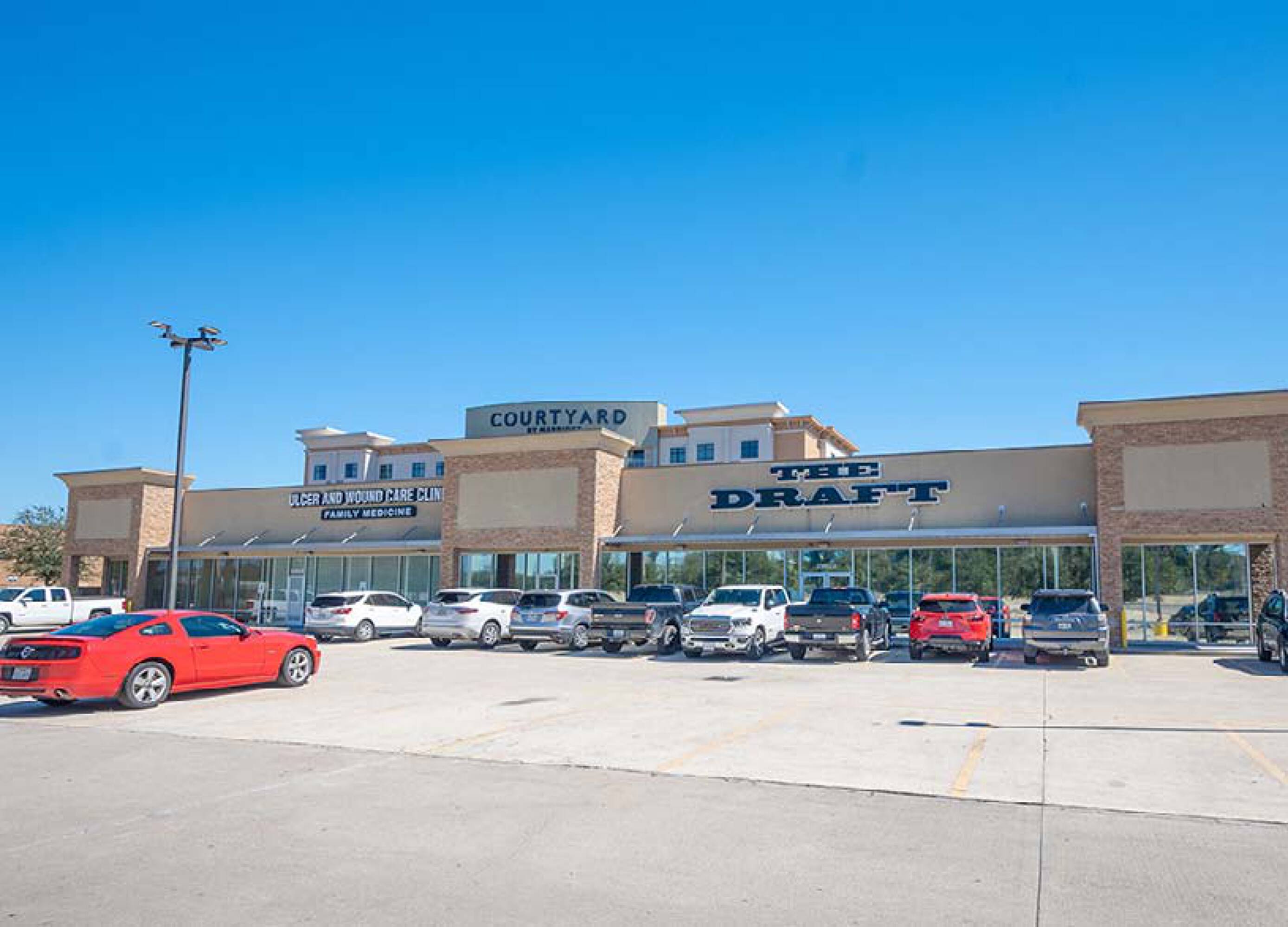 A modern retail strip center with ample parking and prominent signage for Courtyard and Draft.