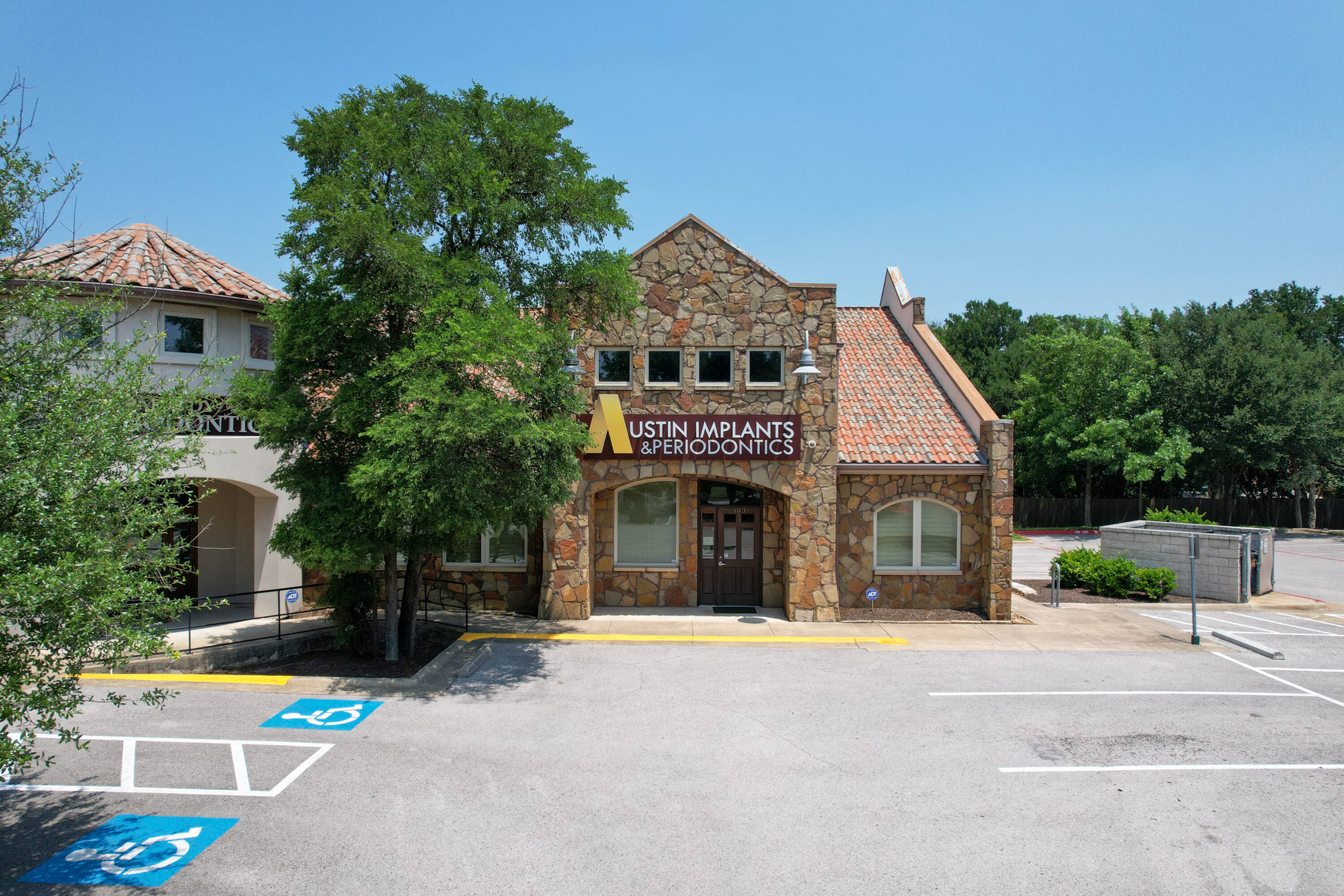 Front view of a two-story dental office building with stone facade and surface parking lot.