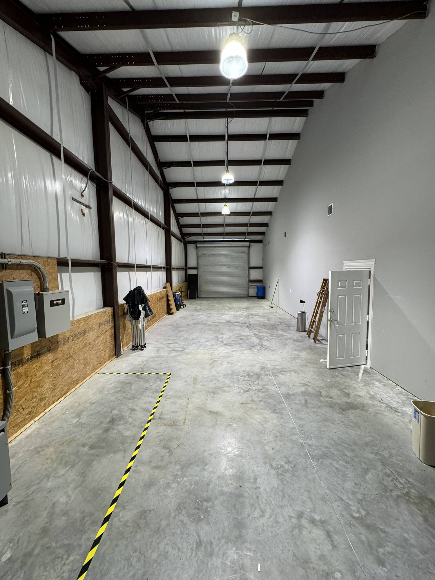 Interior view of an industrial office warehouse with high ceilings, overhead lighting, and a large loading door.