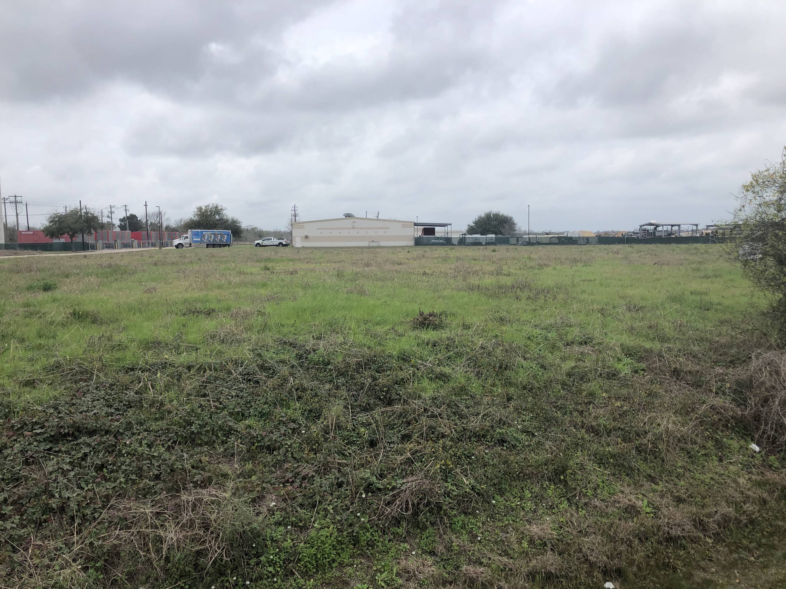 A large, open grassy field with industrial buildings in the background at 3200 Main St., Pearland, TX.