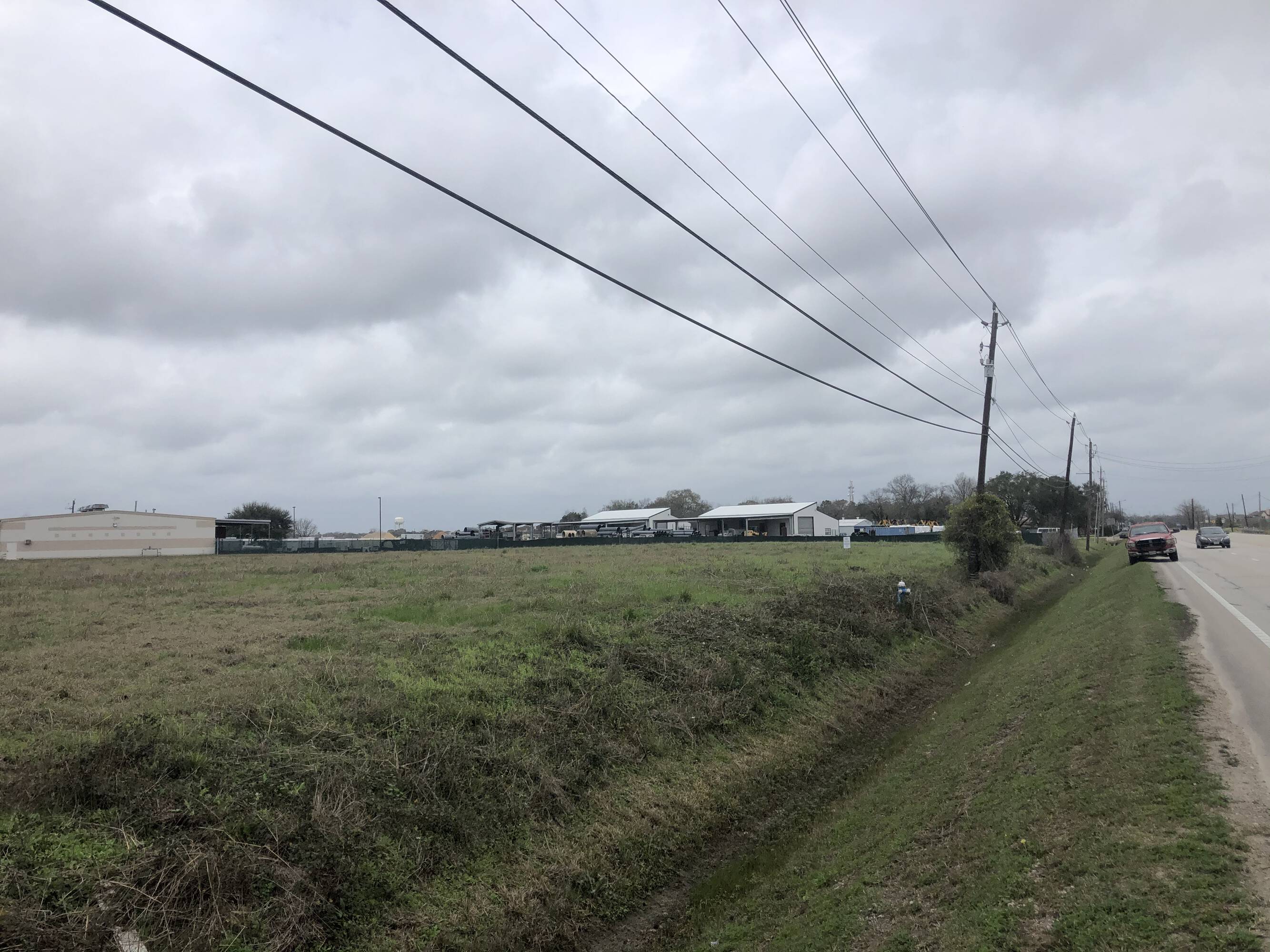 Image of vacant land at 3200 Main St., Pearland, TX, with industrial buildings in the background.