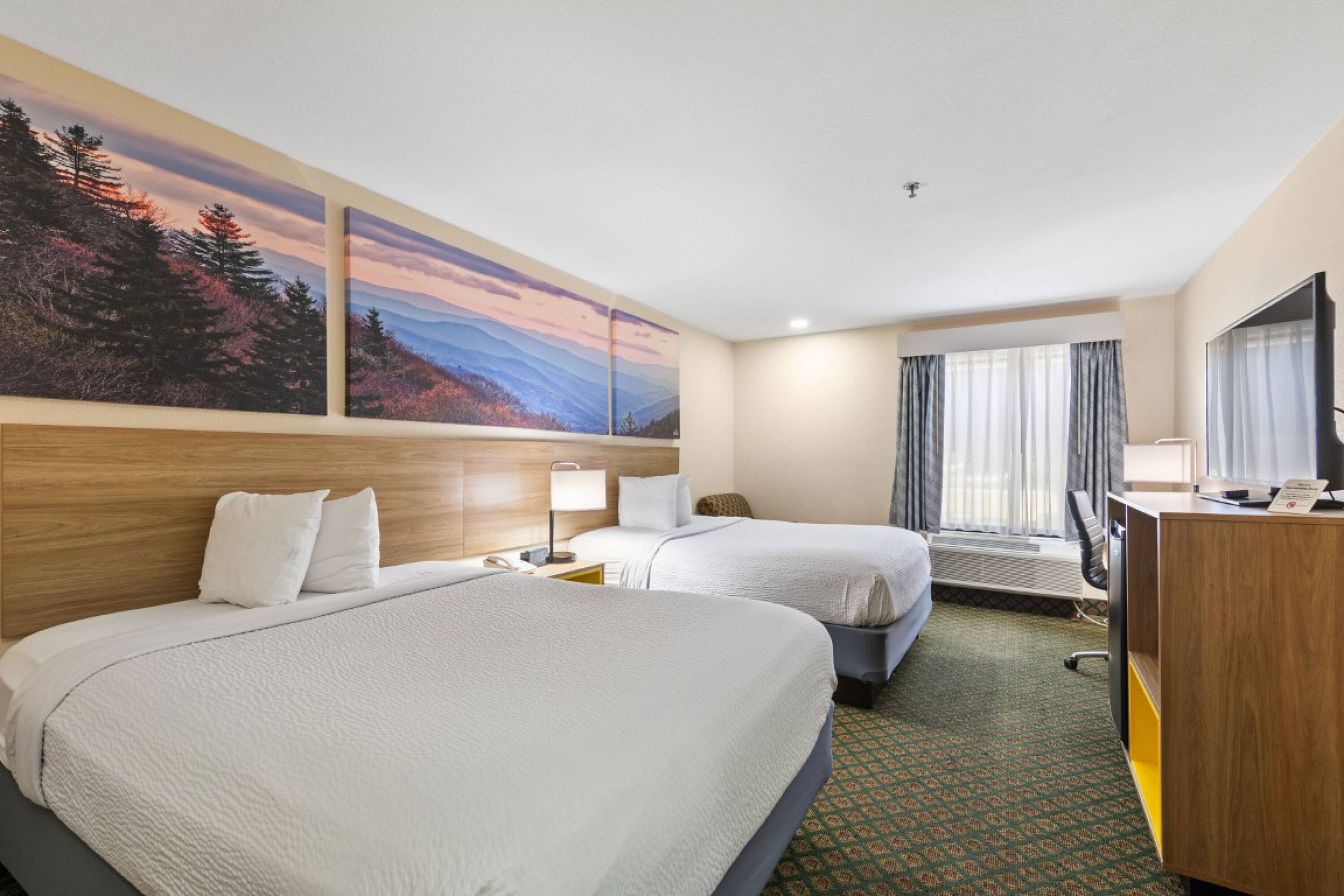 A hotel room at Days Inn & Suites by Wyndham Eunice featuring two queen-sized beds, large windows, and scenic wall murals.