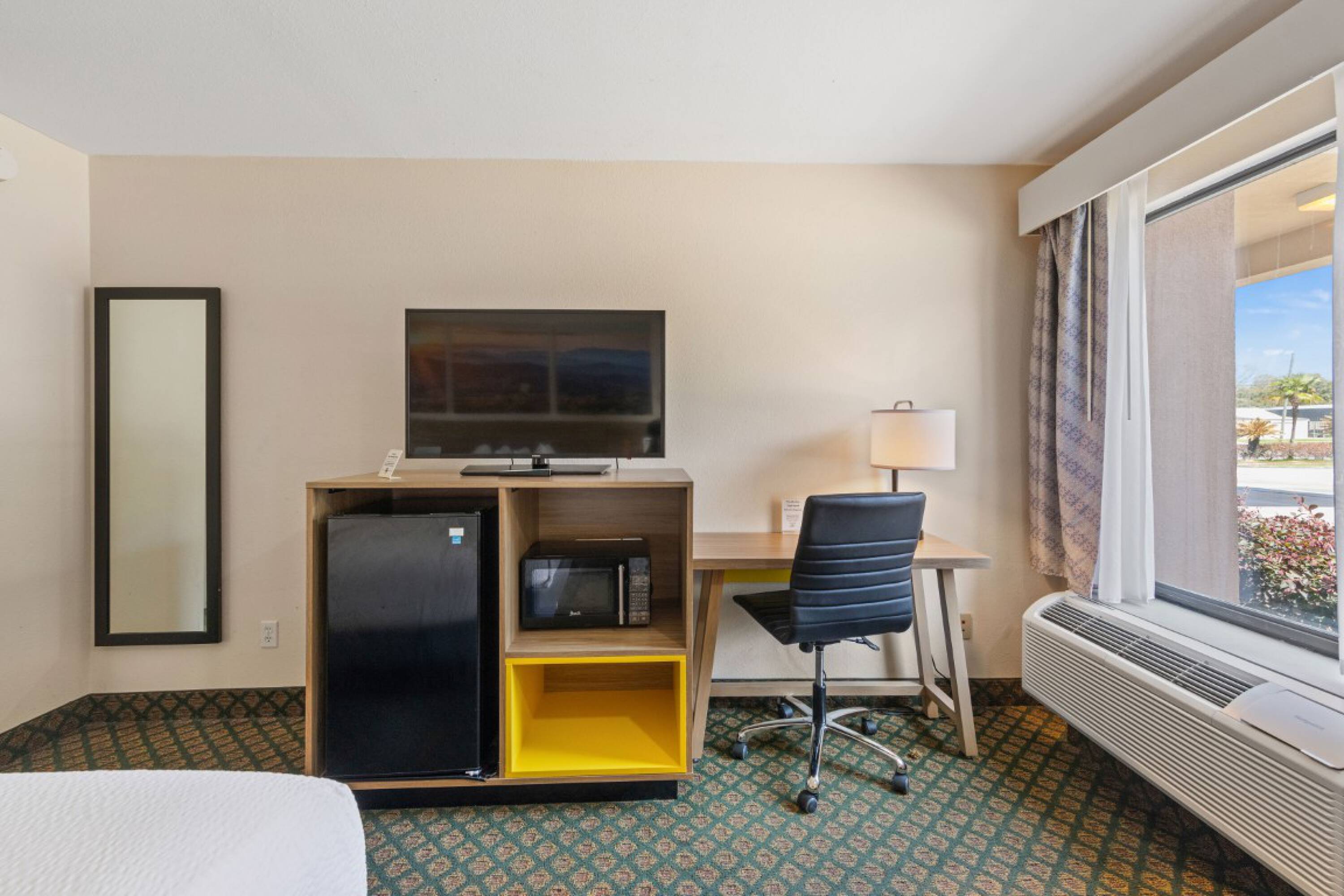 Interior view of a hotel room at Days Inn & Suites by Wyndham Eunice featuring a workspace, refrigerator, microwave, and large window.