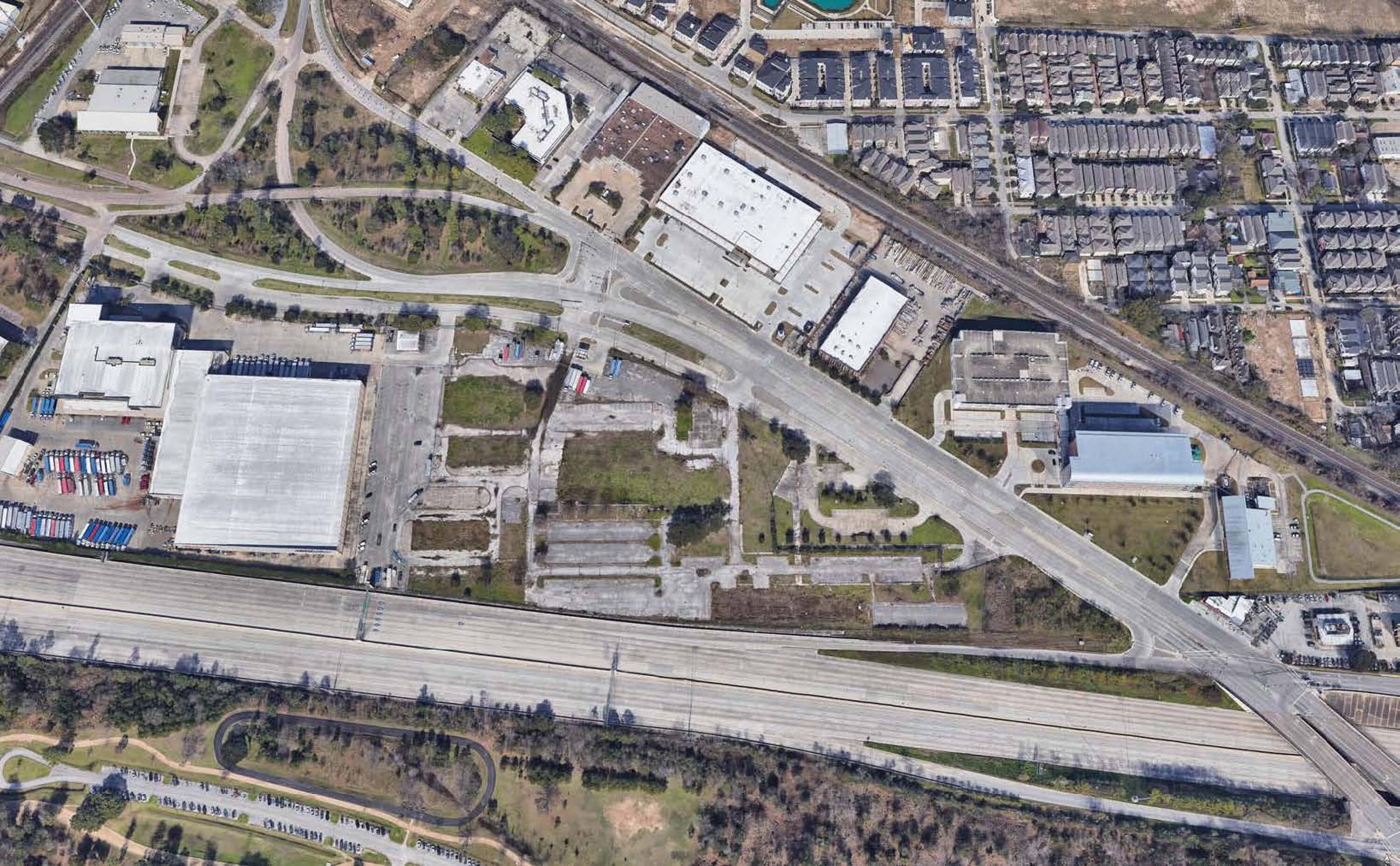 Aerial view of 7701 Washington Avenue, Houston, TX, showing vacant land with adjacent industrial buildings and surrounding neighborhood.