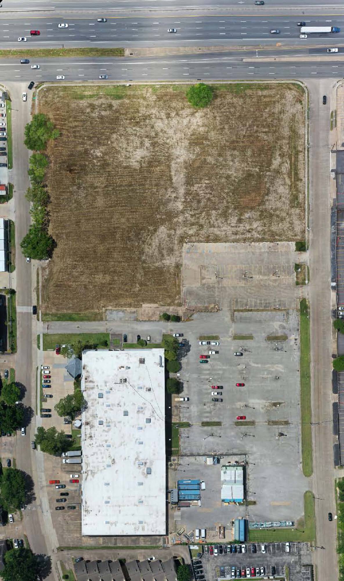 Aerial view of 6767 SW Freeway, Houston, TX, showing vacant land next to a commercial building with parking and loading areas.