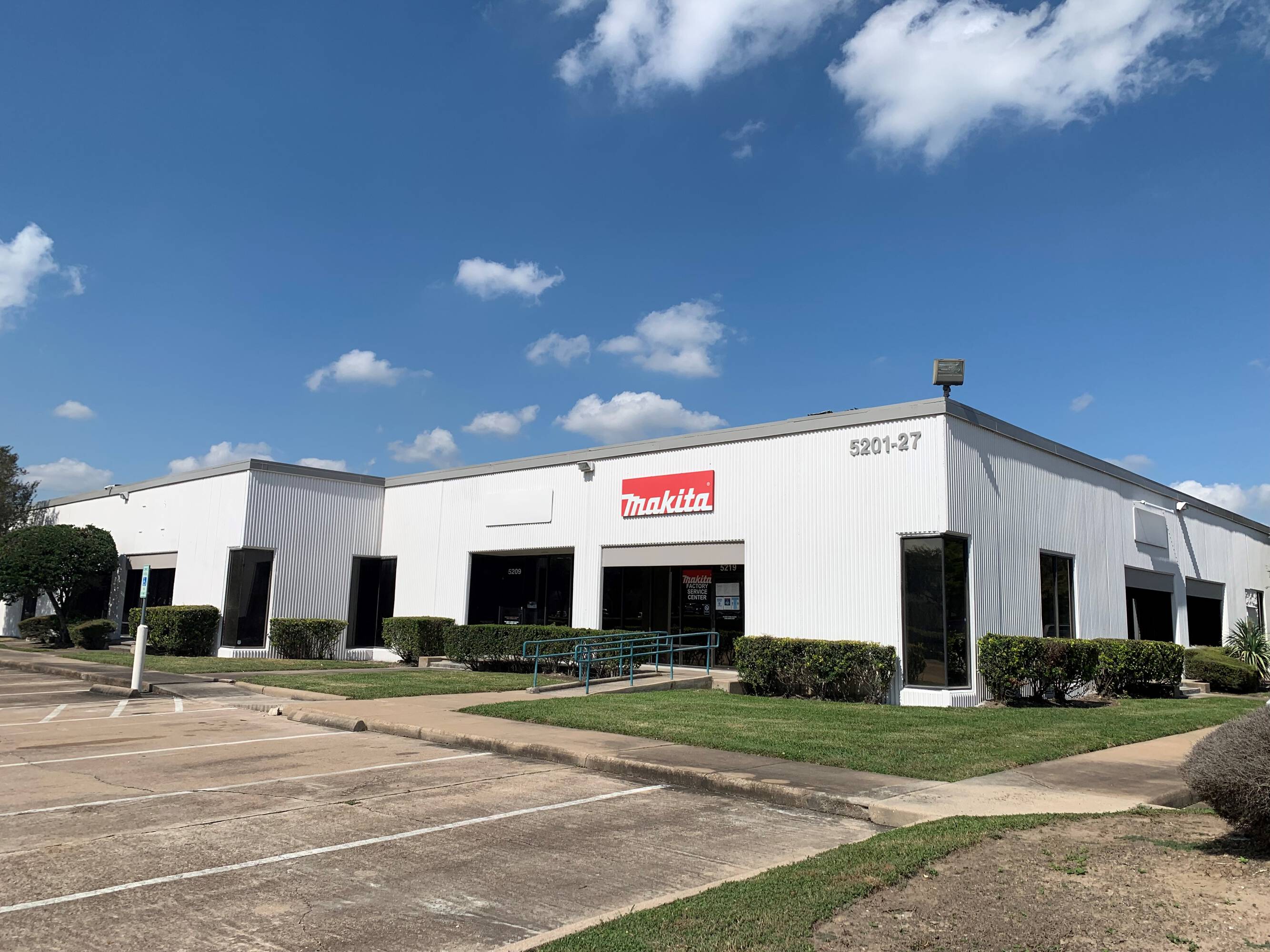 A single-story industrial/commercial building with large windows, surface parking, and a loading dock, featuring Makita signage.