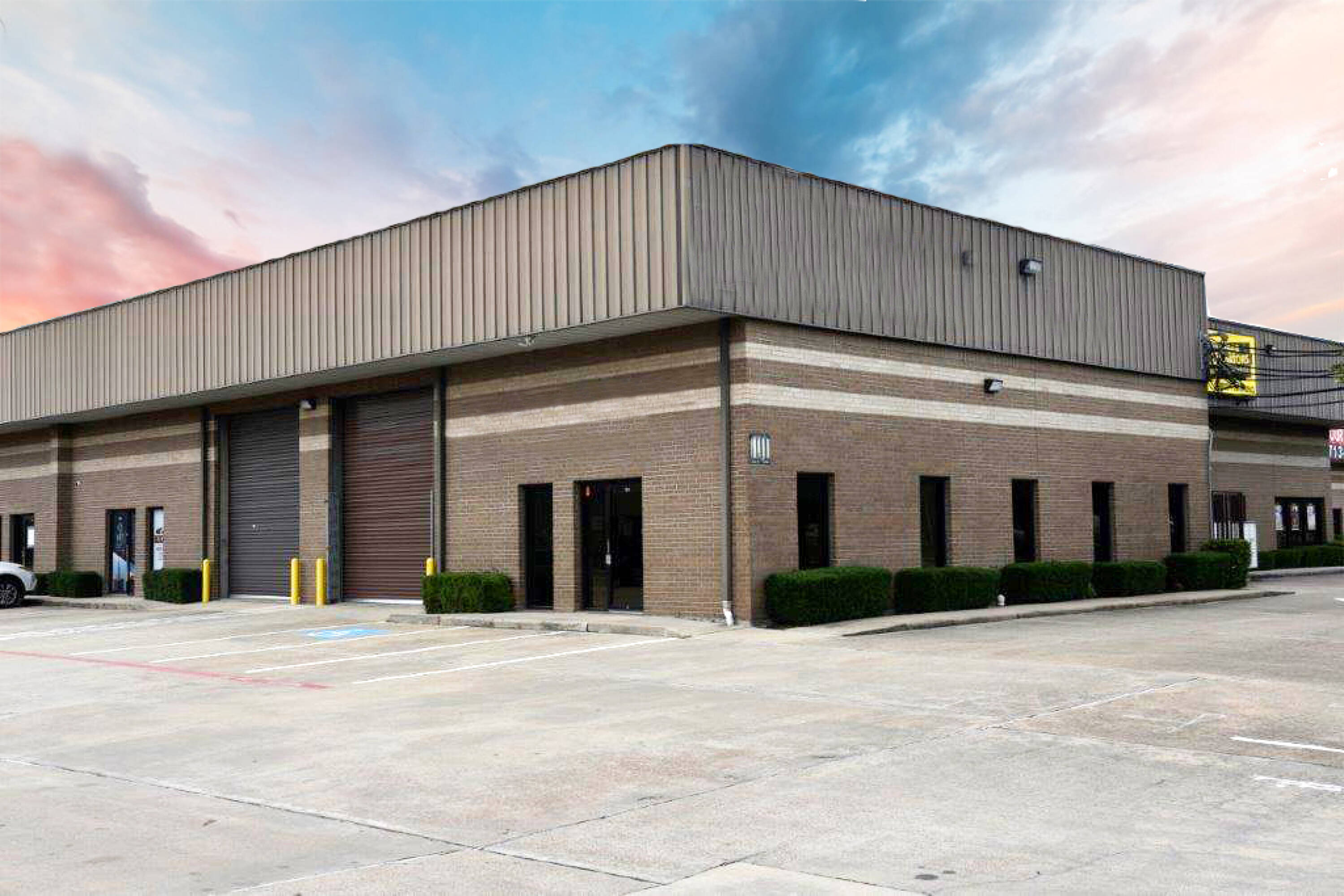 Modern industrial building with brick facade, large loading doors, and ample surface parking.