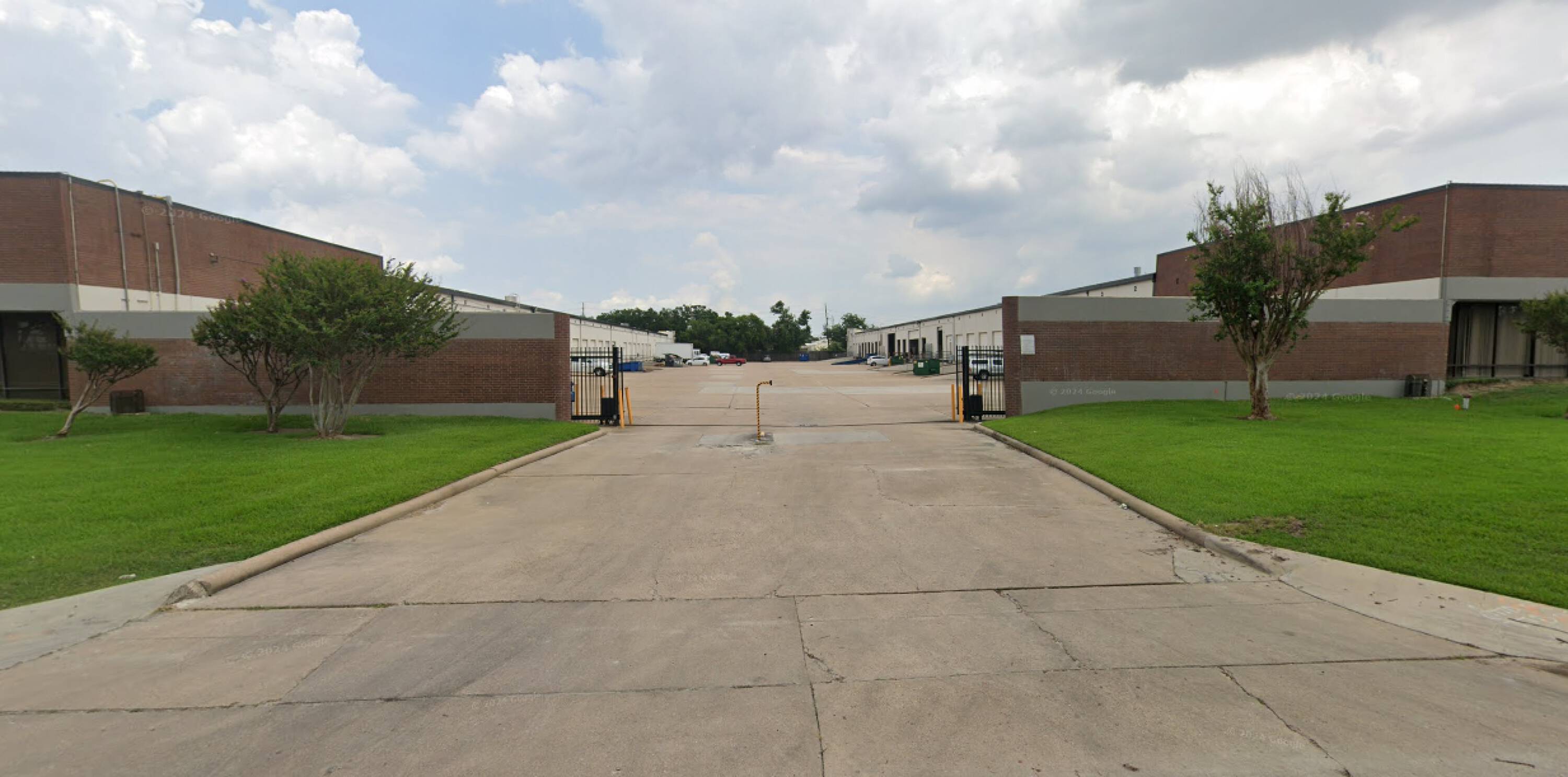Front view of a well-maintained industrial property with brick buildings, security gates, and ample parking.