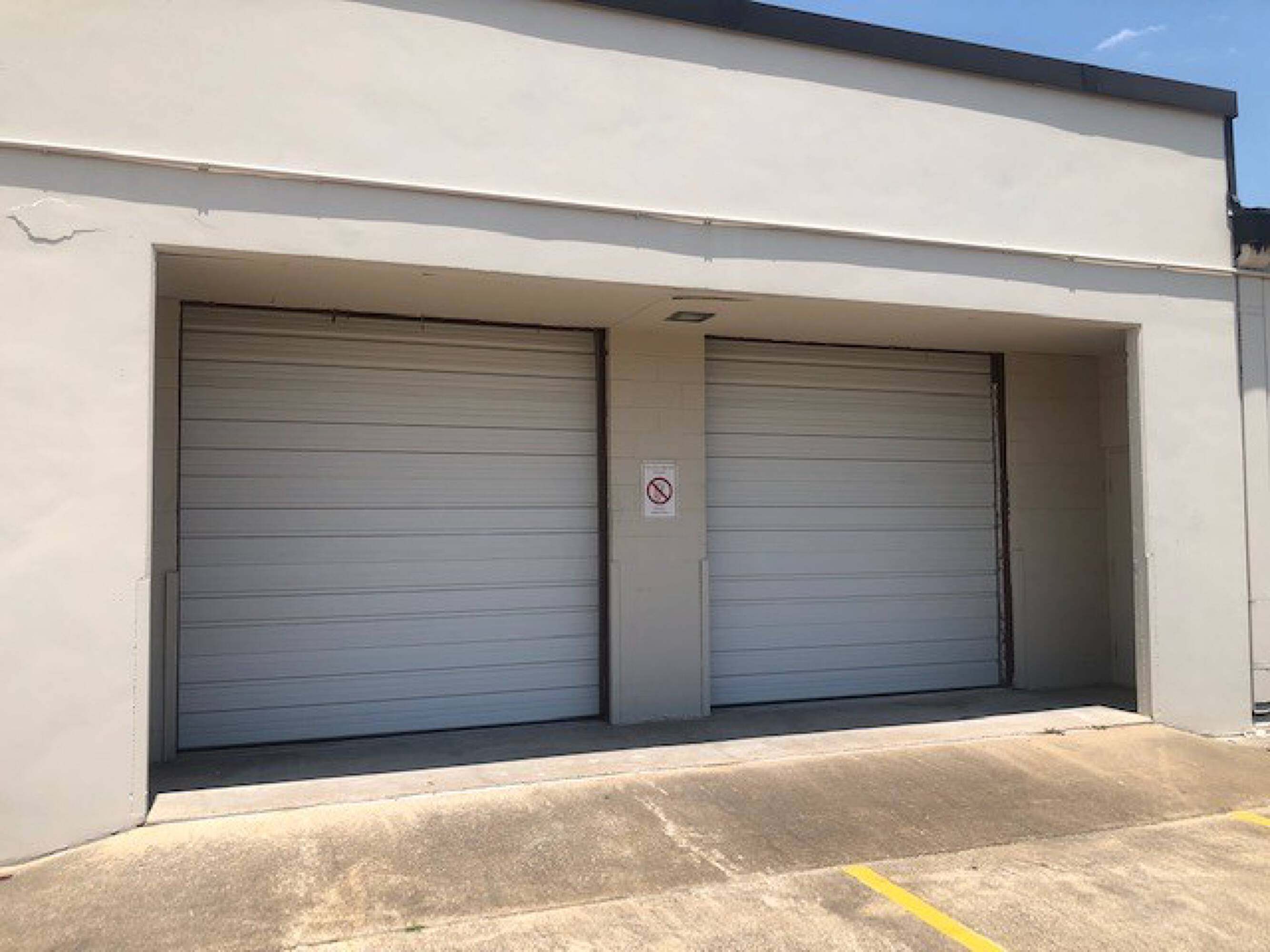 Industrial building with two large roll-up doors for loading and unloading, featuring concrete block construction and surface parking.