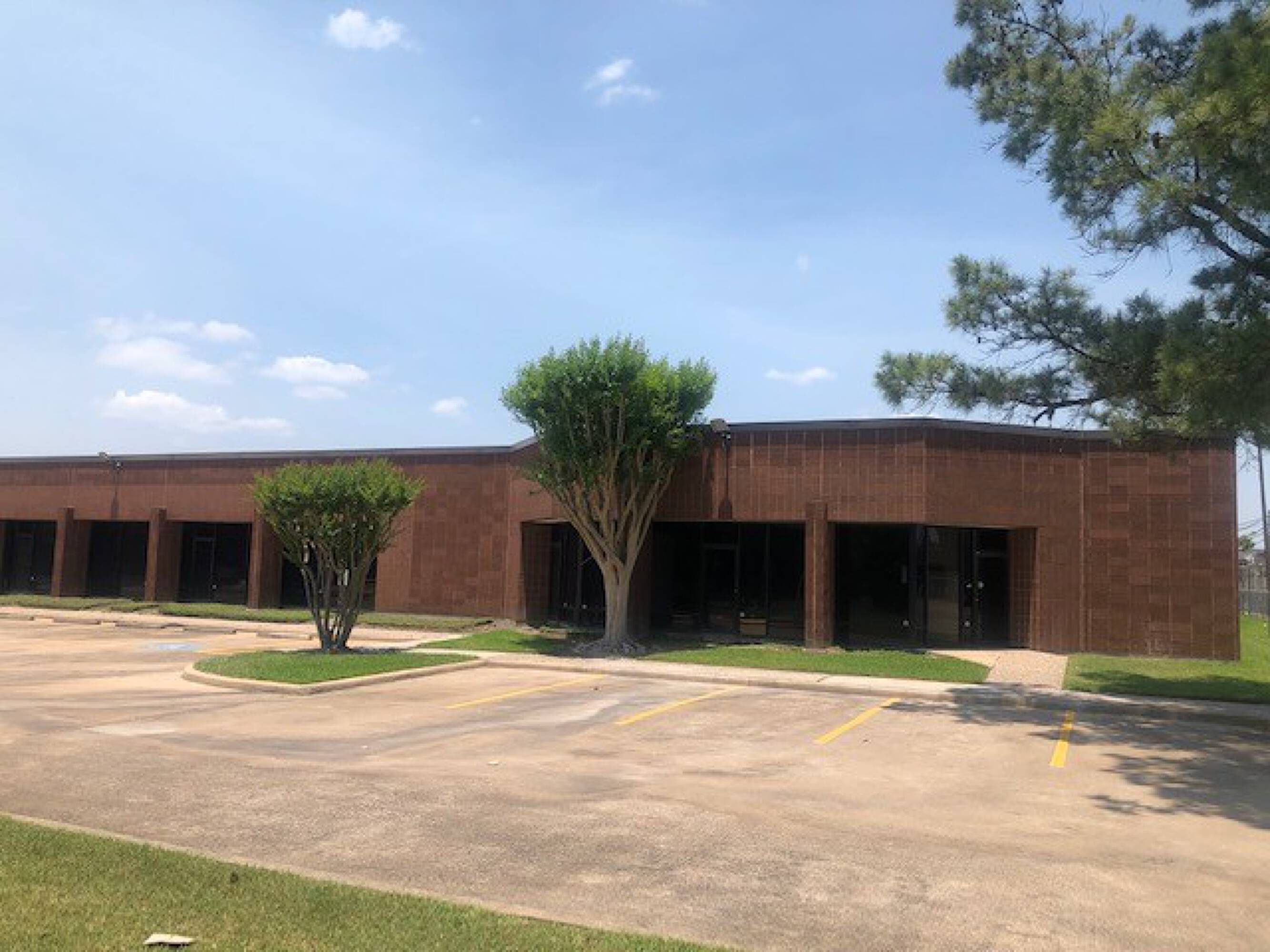 A single-story commercial building with brick facade, large windows, and surface parking lot.