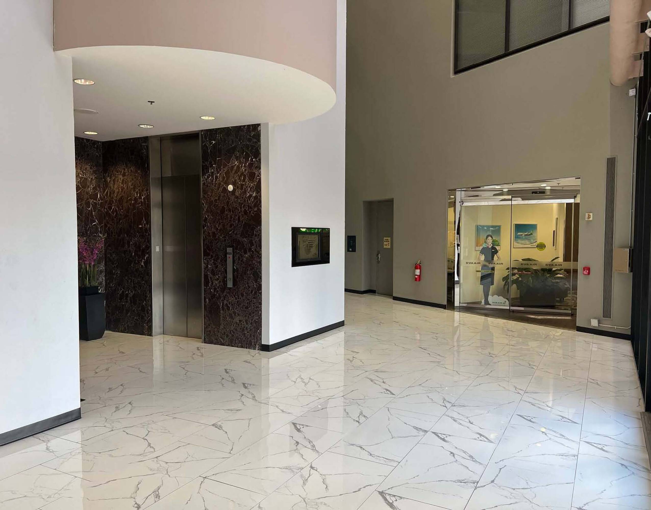 Modern office building lobby with marble floors, large windows, and elevator access.