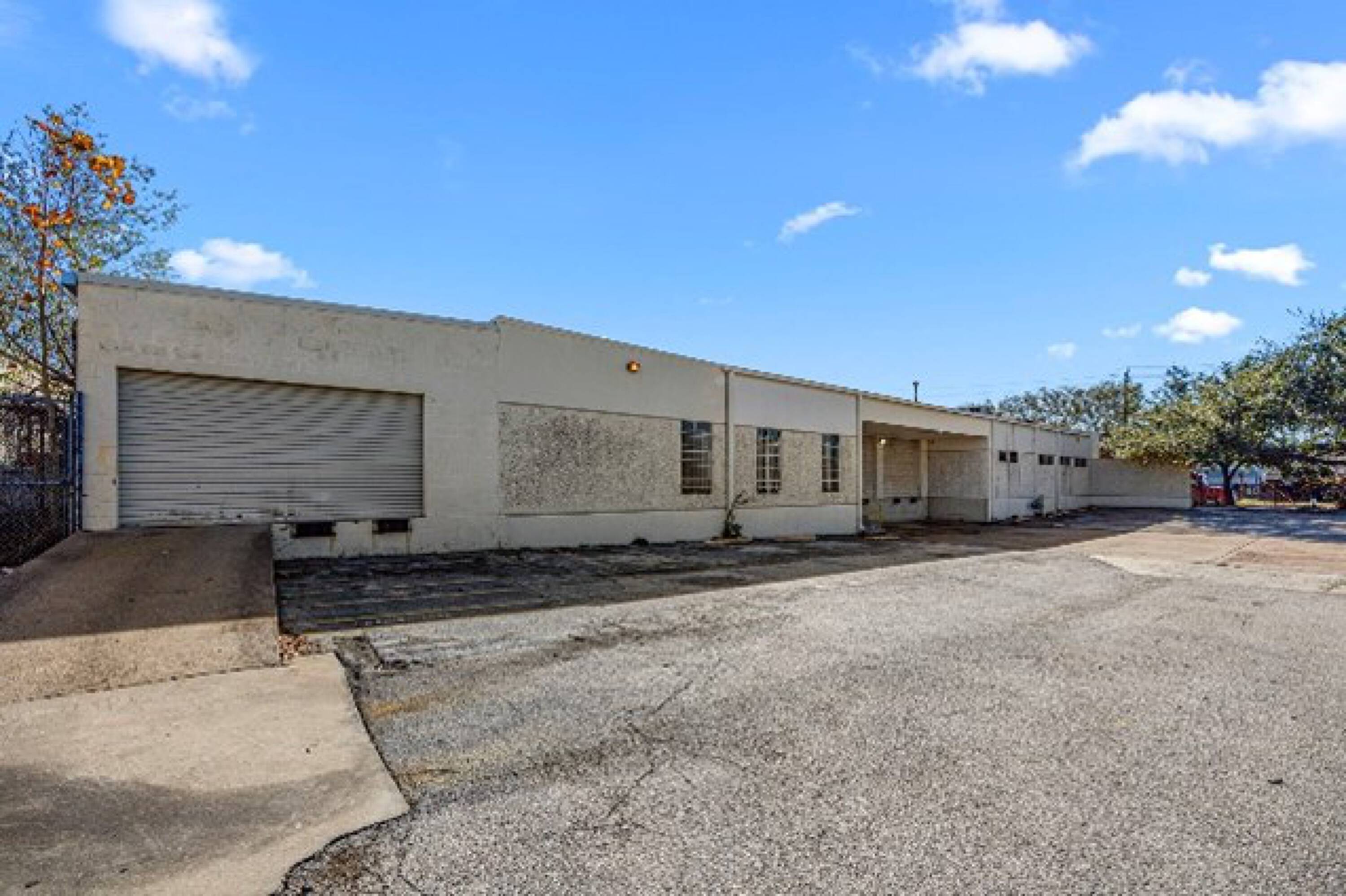 Side view of a single-story industrial warehouse with large roll-up door and surface parking at 6880 Wynnwood Lane, Houston, TX.