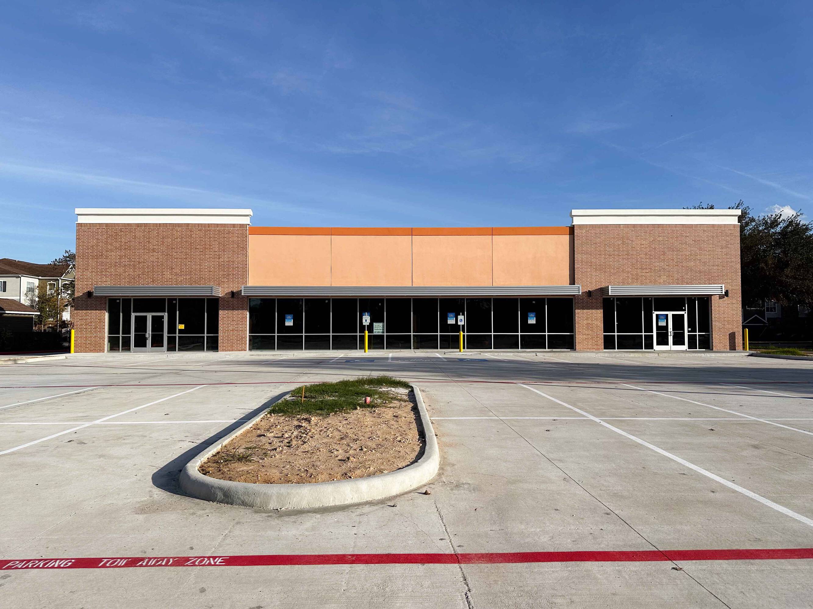 The Shoppes at Riata Heights retail property with a brick facade and large glass windows, ample parking, and a landscaped median.