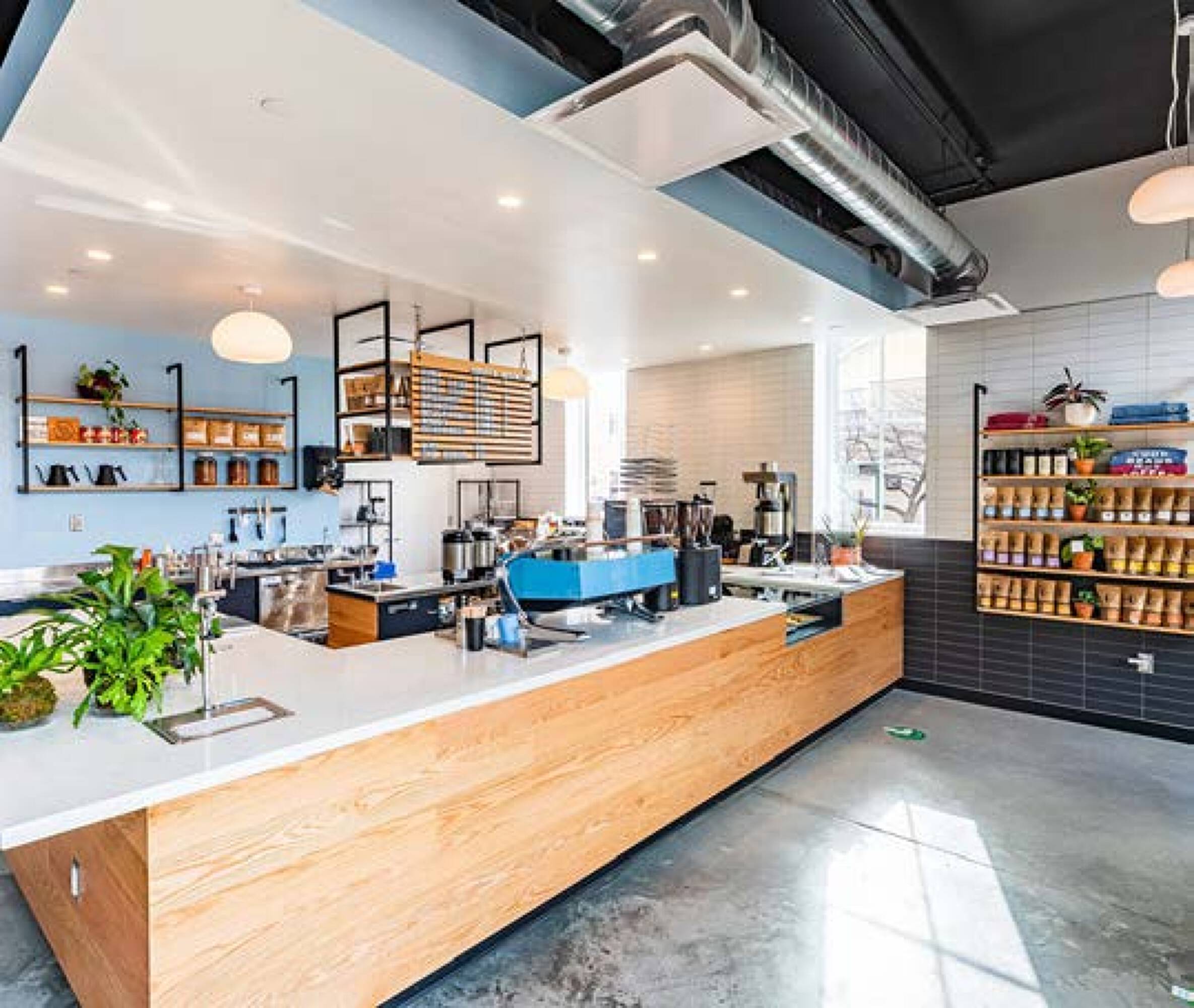 Interior of a modern retail space with a coffee shop setup, featuring large windows, natural light, and a central service counter.