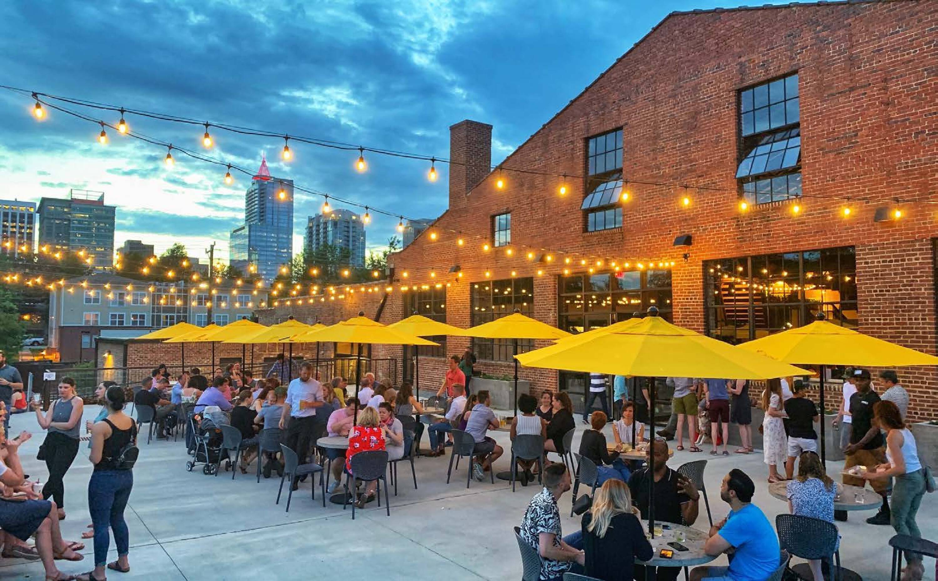 Outdoor dining area with yellow umbrellas and string lights at The Bend in Humble, TX.