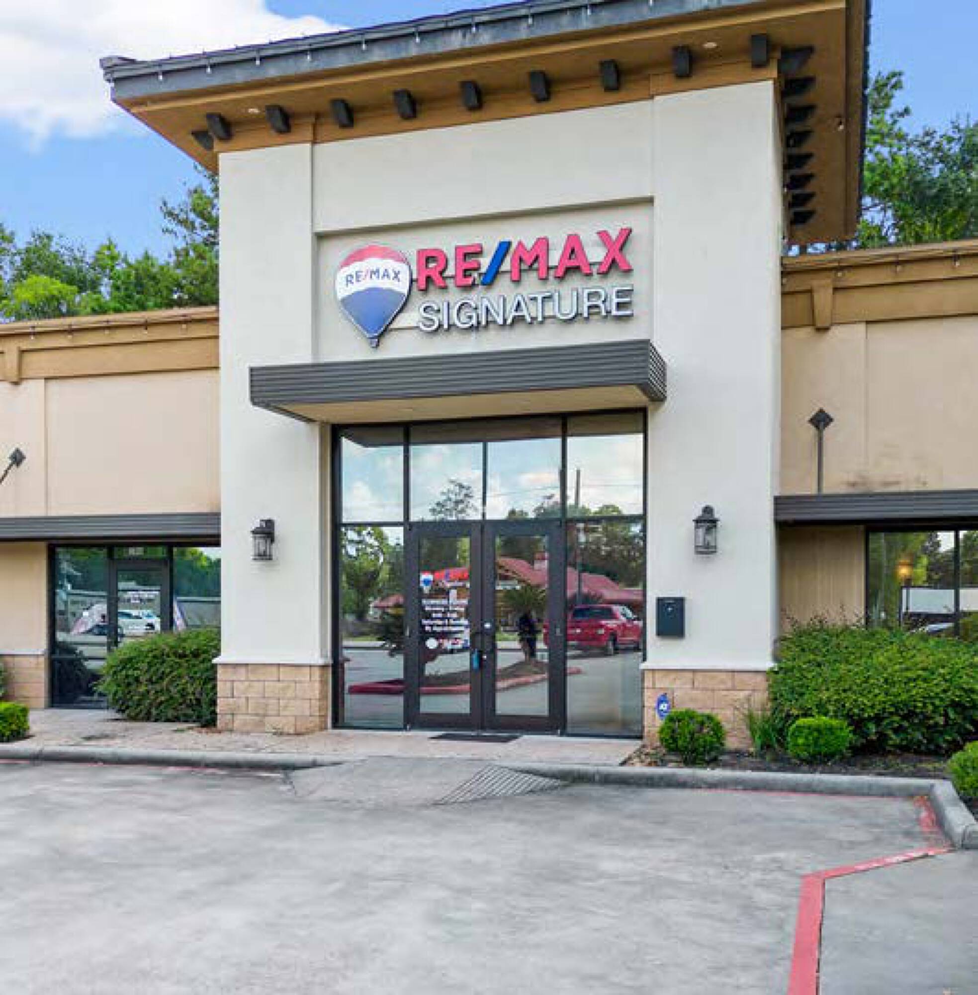 Tuscan Village Plaza retail space with large windows, stucco exterior, and RE/MAX Signature signage.