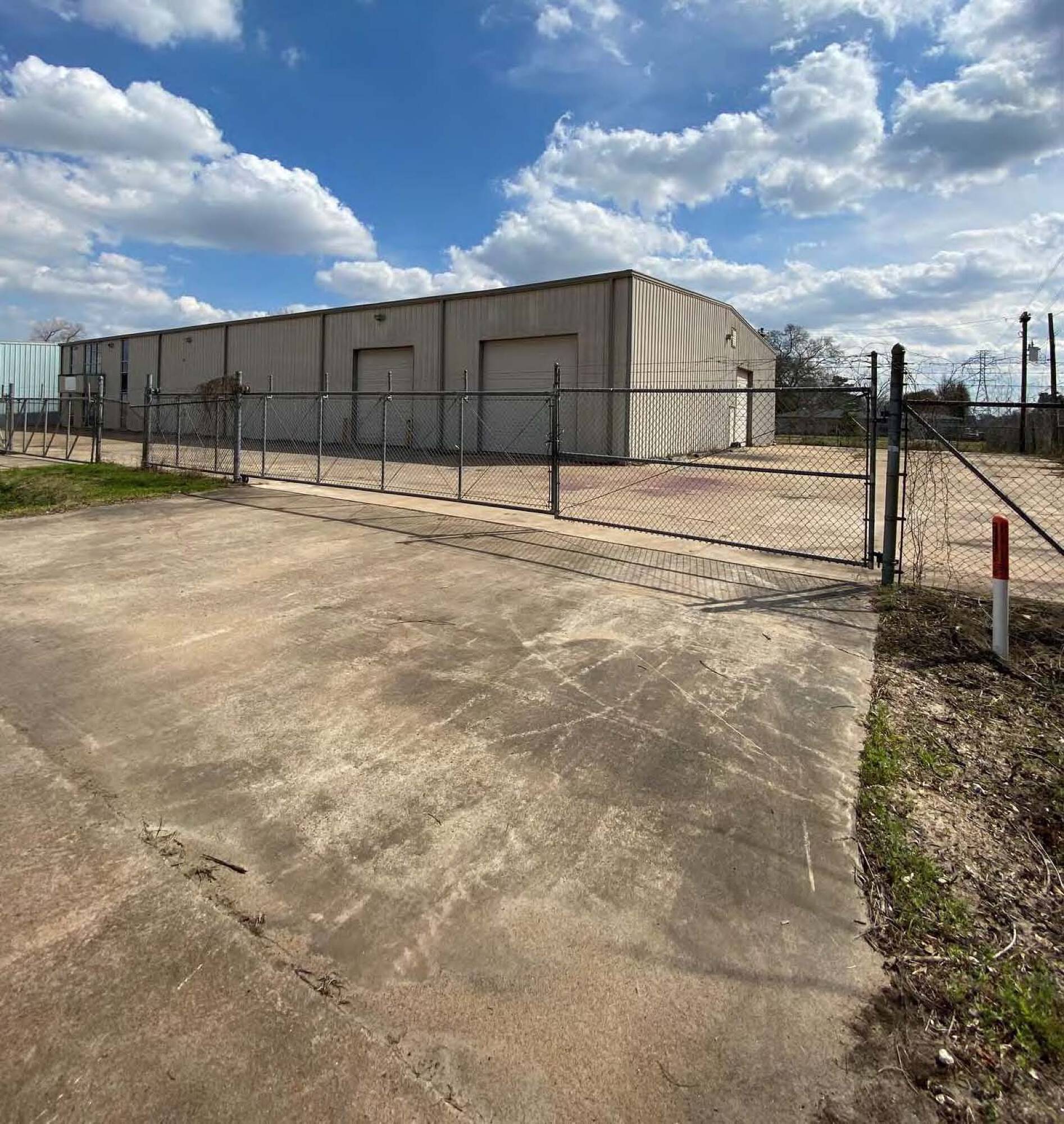 Industrial warehouse with secure fencing, large loading doors, and ample parking space.