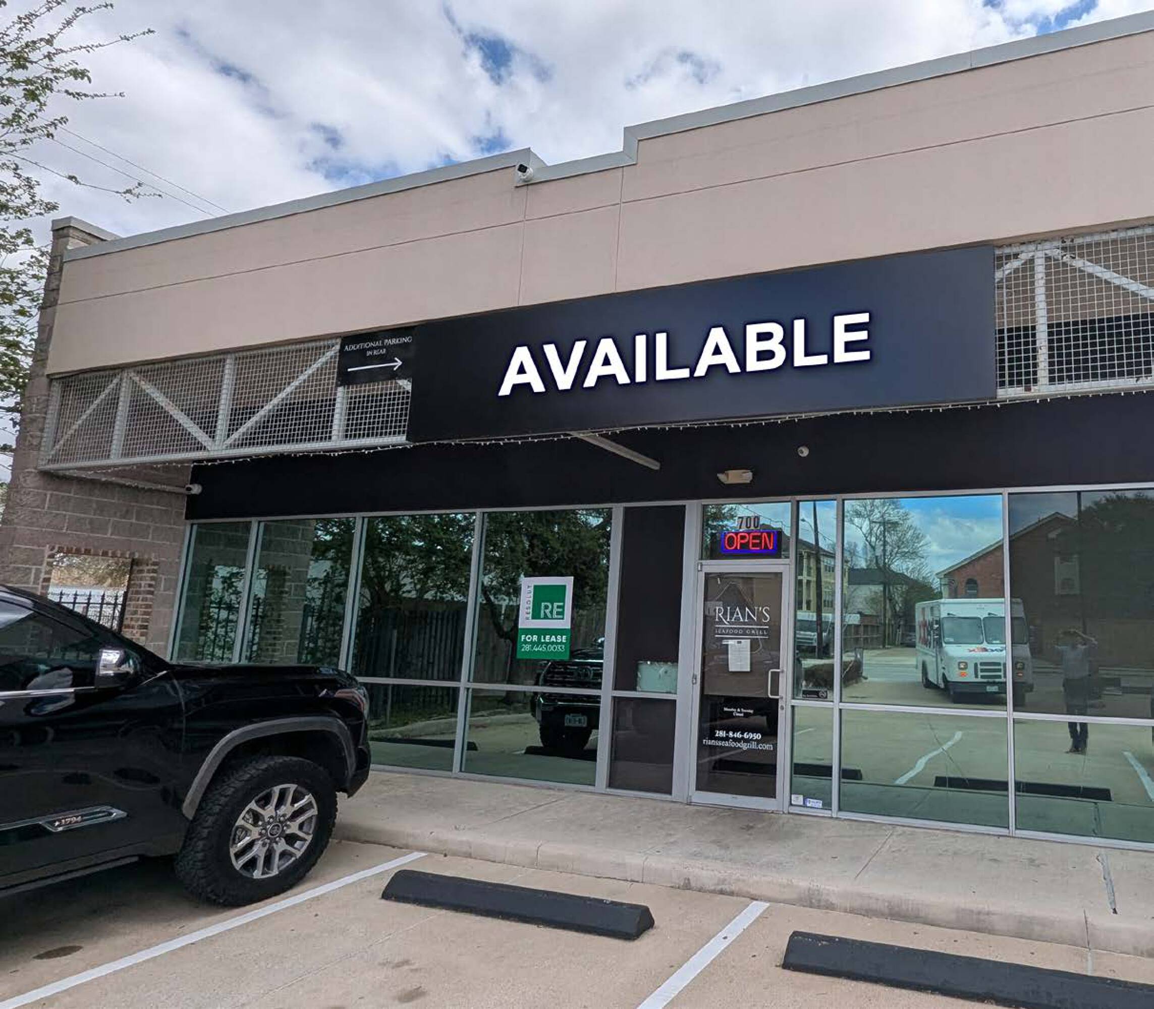 Commercial property with large glass windows, surface parking, and a "For Lease" sign indicating availability.