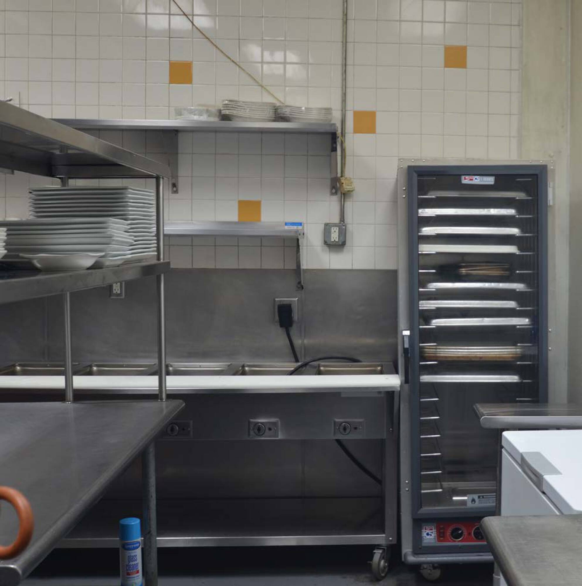 Industrial commercial kitchen with stainless steel counters, high ceilings, and modern equipment.