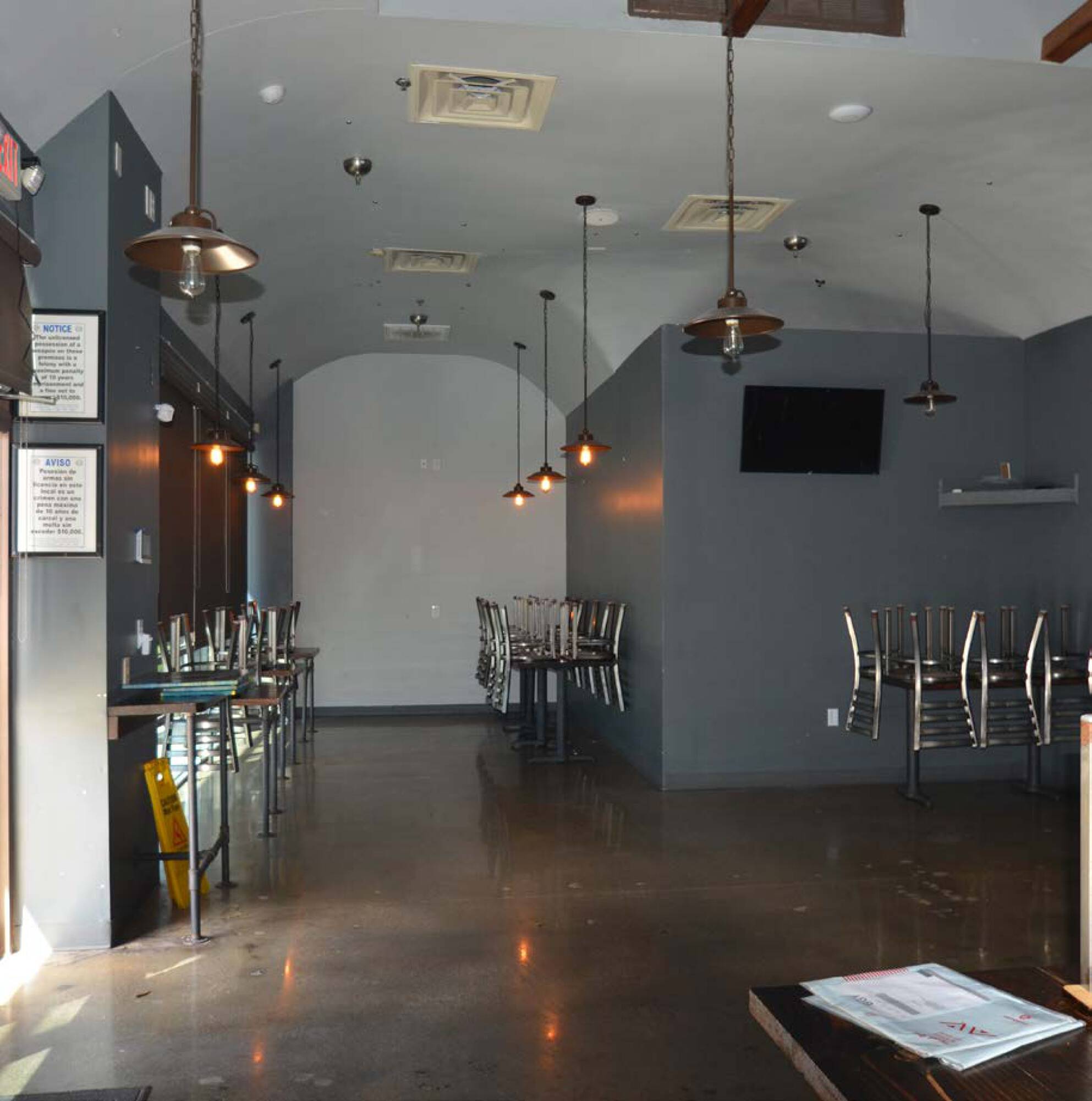 Modern restaurant or bar interior with high ceilings, industrial lighting, and open seating areas.