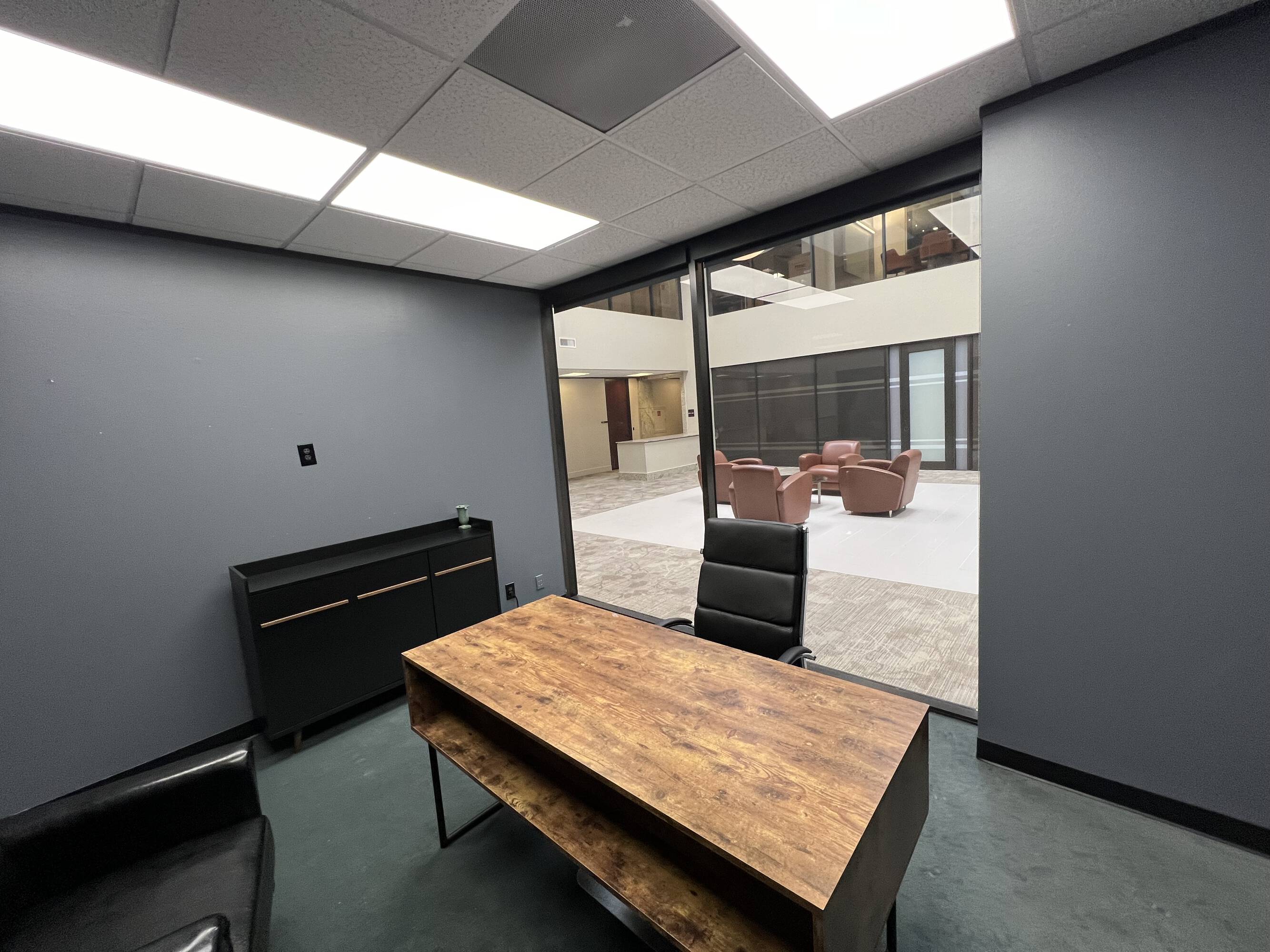 Office space with large windows, modern lighting, and a view into an atrium area.