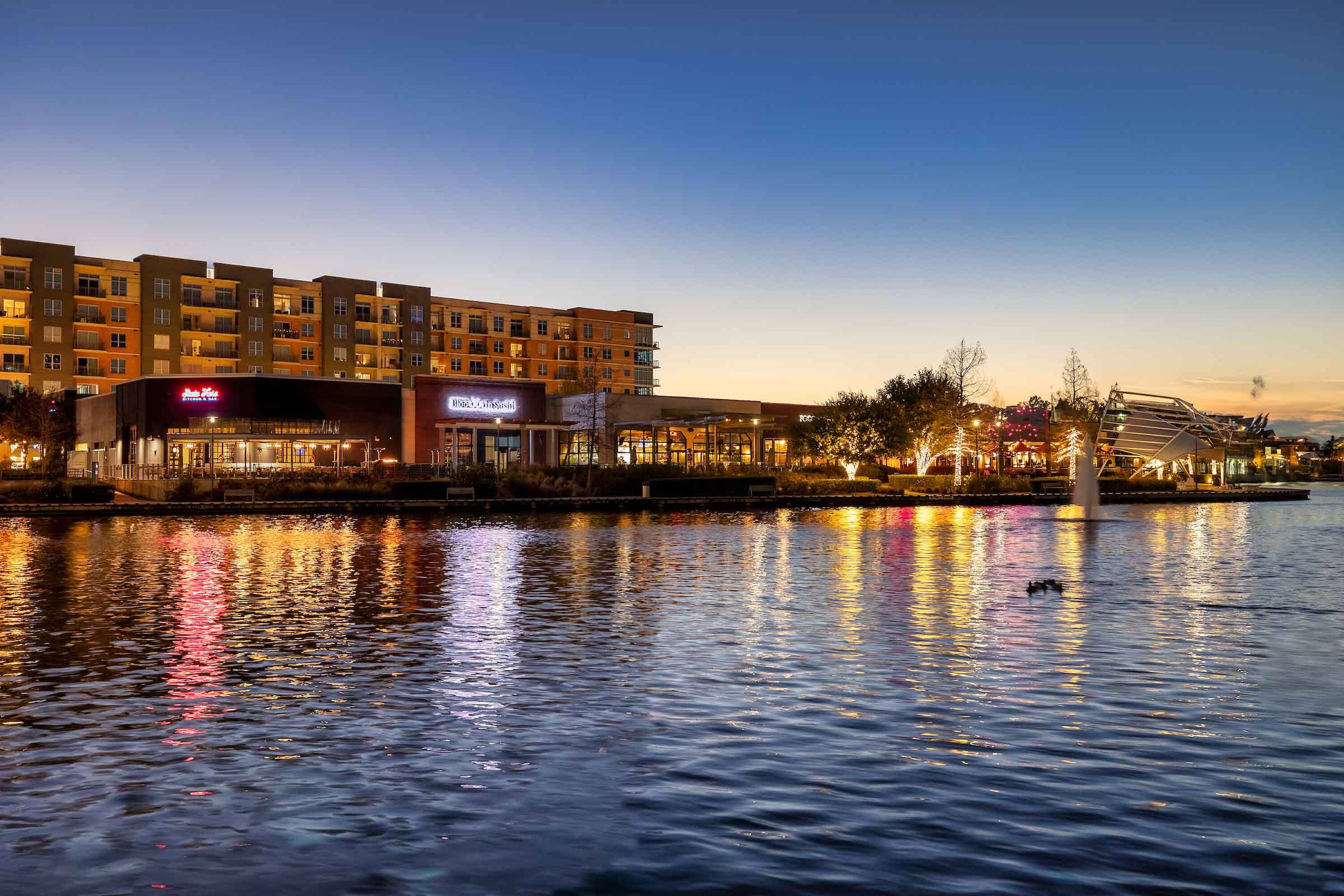 Evening view of Hughes Landing on Lake Woodlands with retail stores along the waterfront.