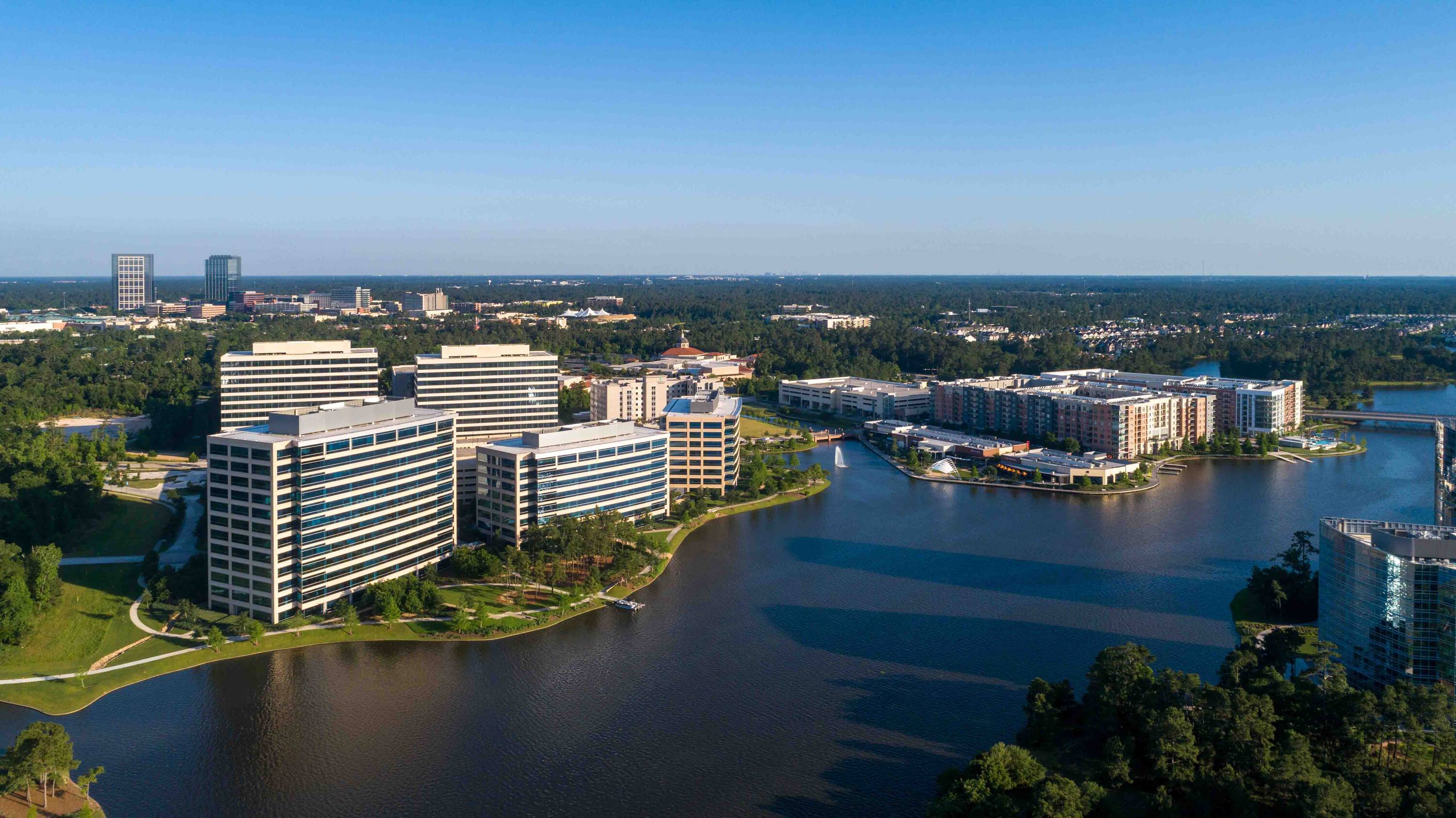 Aerial view of Hughes Landing on Lake Woodlands, showcasing modern retail buildings with waterfront views and extensive parking.
