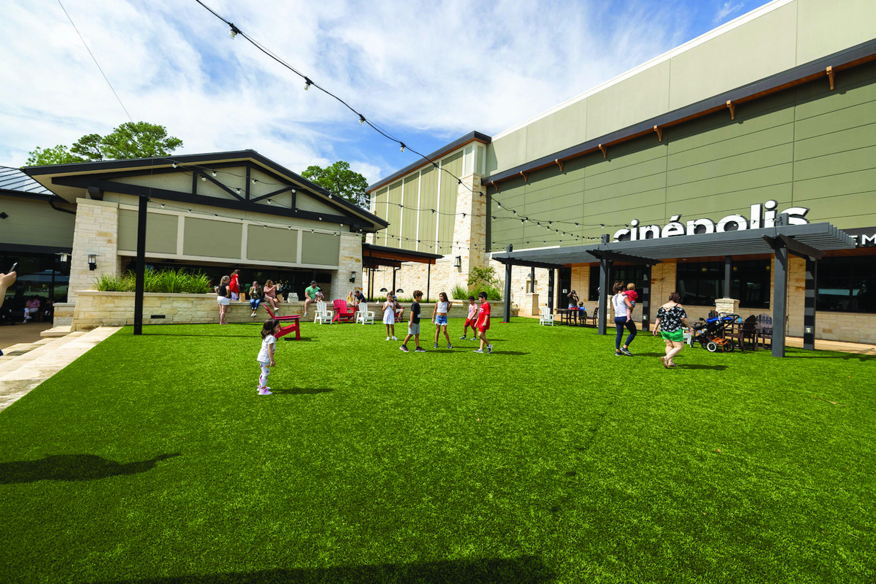 Outdoor green space with children playing in front of a retail center featuring Cinépolis cinema in Spring, TX.